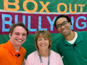 School psychologist Lisa Goff and two presenters smile in front of the Box Out Bullying sign
